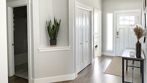 Un pasillo amplio con suelo de madera, paredes blancas y una planta en maceta.
