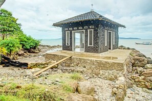 A stone building with a tiled roof near a rocky shoreline. - OYO 90279 Wartawan De Mansion (Kalianda)