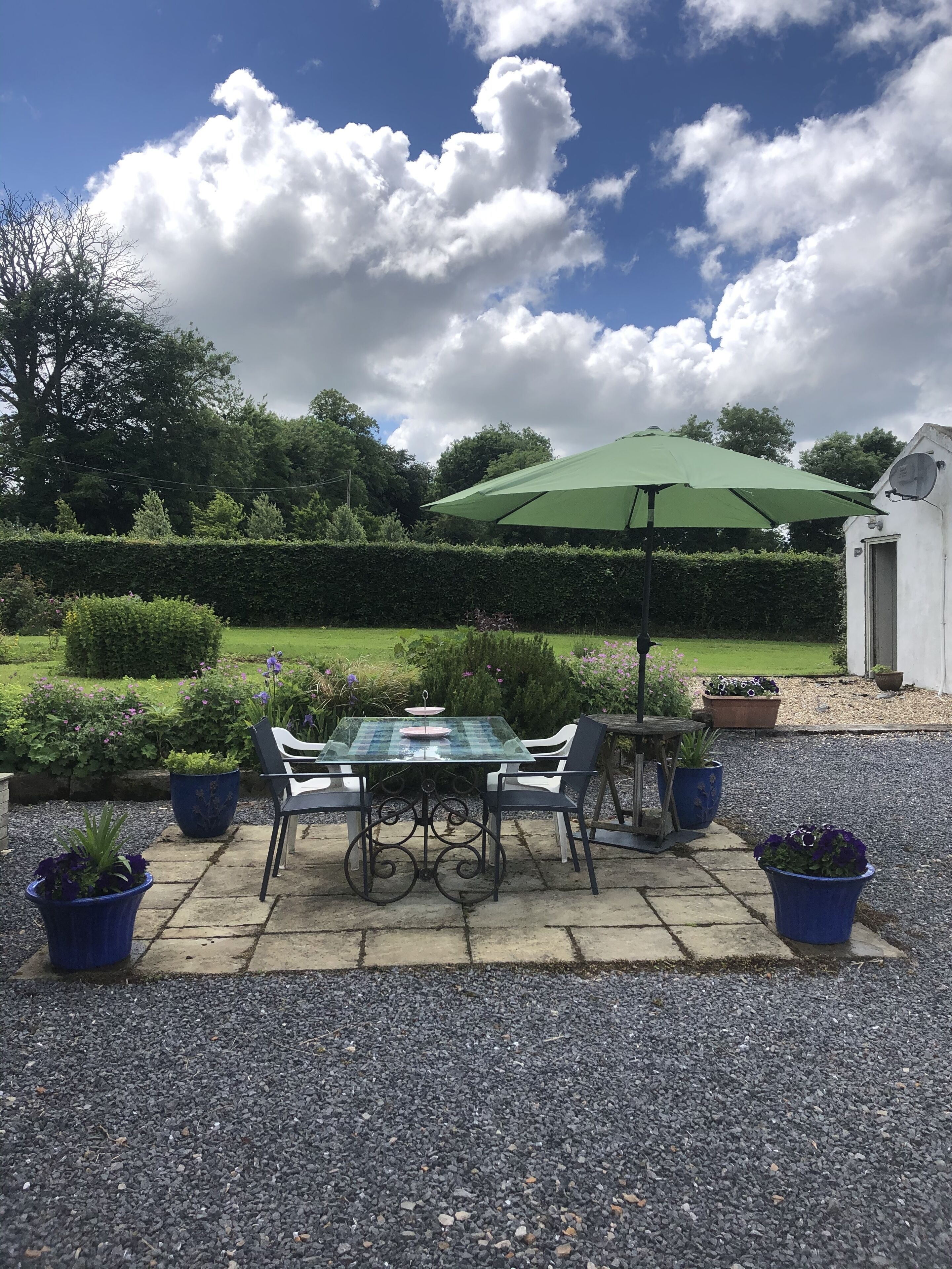 A patio with a table and chairs, surrounded by potted plants and a hedge.