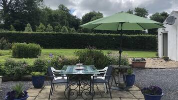 A patio with a table and chairs, surrounded by potted plants and a hedge.