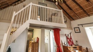 A rustic room with a wooden ceiling, a balcony with white railings, and a red curtain. - Irish Thatched cottage. Escape to a piece of living history on a country farm (Knocklong)