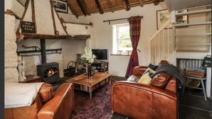 A cozy living room with a fireplace, leather sofas, a coffee table, and a rustic stone floor. - Irish Thatched cottage. Escape to a piece of living history on a country farm (Knocklong)