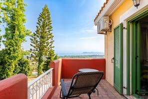A balcony with a view of the sea, a chair, and a door with green shutters.