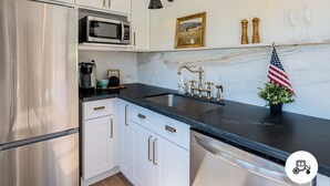 Una cocina moderna con gabinetes blancos, electrodomésticos de acero inoxidable, una encimera negra y una pequeña decoración con la bandera estadounidense.
