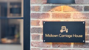 Un muro de ladrillo con un letrero negro que dice "Midtown Carriage House" y una lámpara negra encima.