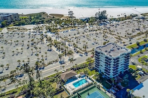An aerial view of a coastal hotel with a parking lot, pool, and beachfront.
