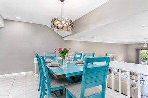 A dining area with a blue table and chairs, a chandelier, and a vase with flowers. - Walk to Siesta Beach, Heated Pool, Tennis, Balcony (Siesta Key)