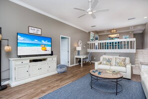 A living room with a TV, white furniture, a ceiling fan, and a staircase leading to an upper level. - Across the Street to Siesta Key Beach, Tennis. Pickleball, Park, Heated Pool | Waterfront Balcony! (Siesta Key)