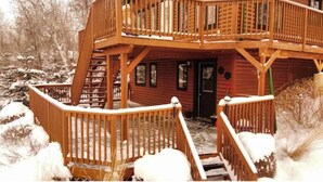 A wooden cabin with a two-story deck and a staircase leading to the entrance.