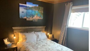 A bedroom with a bed, two bedside lamps, a nightstand, and a framed picture on the nightstand.