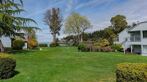 A residential property with a well-maintained lawn, mature trees, and a view of a body of water. - Ocean View Hideaway Suite B (Nanoose Bay)
