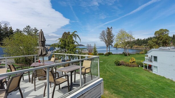 A deck with outdoor furniture, a clear view of a lake, and a grassy area with trees. - Ocean View Hideaway Suite B (Nanoose Bay)