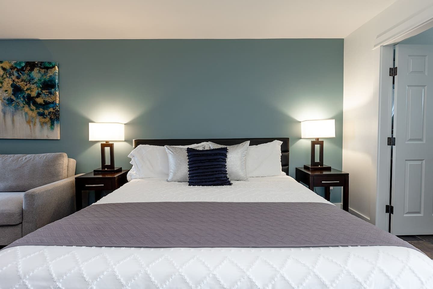 Une chambre d’hôtel avec un lit, deux tables de chevet avec des lampes, un canapé et un tableau au mur.