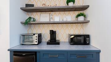 Una cocina con tostadora, cafetera y microondas sobre una encimera azul, y repisas decorativas arriba.