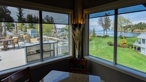 A room with large windows overlooking a patio area with outdoor furniture and a view of a lake. - Ocean View Hideaway Suite B (Nanoose Bay)