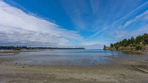 A beach with a clear sky, calm water, and a distant shoreline. - Ocean View Hideaway Suite B (Nanoose Bay)