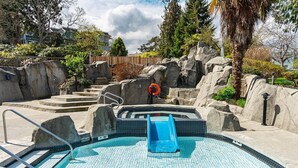 A swimming pool with a blue slide, stone steps, and a lifeguard stand. - Ocean View Hideaway Suite B (Nanoose Bay)
