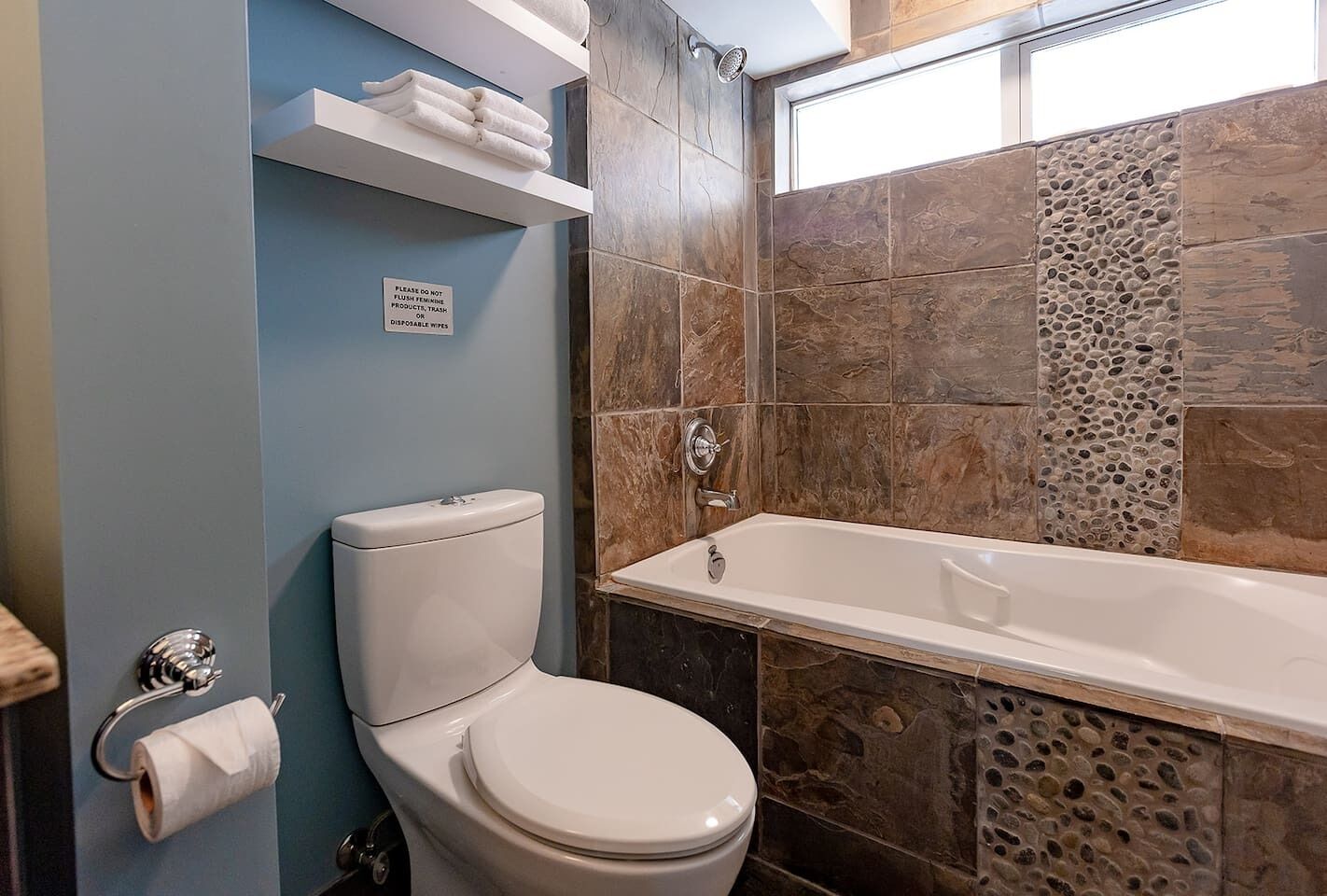 Een badkamer met een toilet, een douche en een bad. Er hangt een bord aan de muur en er liggen handdoeken op een plank.