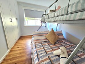 A bunk bed with striped bedding, a teddy bear, and a window with blinds. - Luxurious 2BR: Near Showgrounds & Racecourse! (Moonee Ponds)
