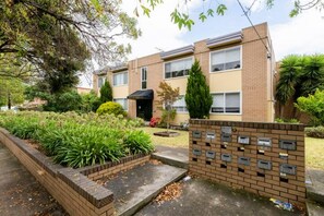 A two-story apartment building with a brick facade, a small front garden, and a mailbox. - Luxurious 2BR: Near Showgrounds & Racecourse! (Moonee Ponds)