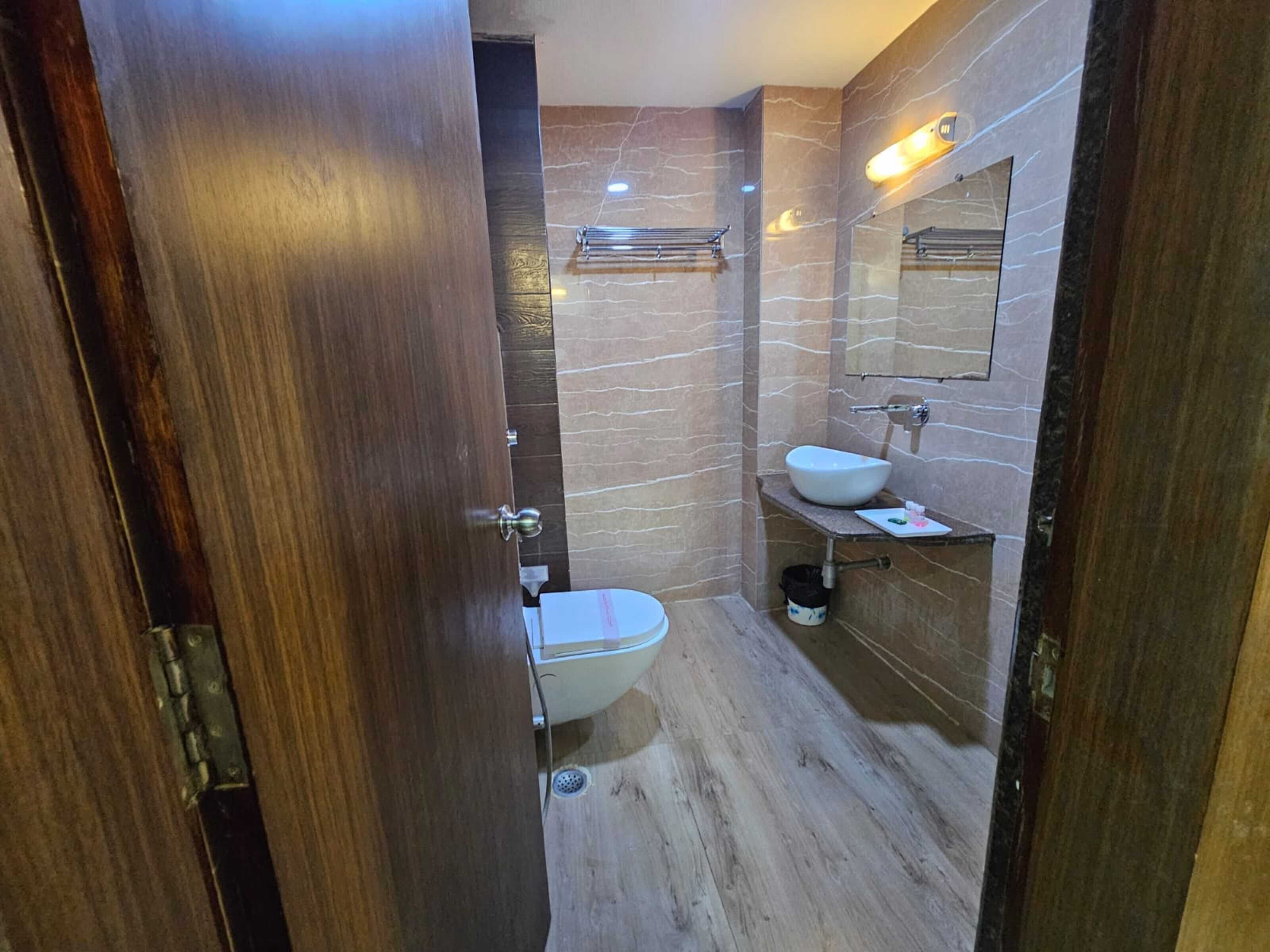 Een moderne badkamer met een houten deur, een wit toilet, een wastafel met een marmeren blad en een spiegel boven de wastafel.