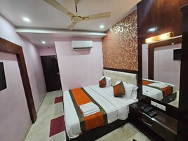 A hotel room with a bed, a ceiling fan, an air conditioning unit, a bedside table with a phone, and a mirror.