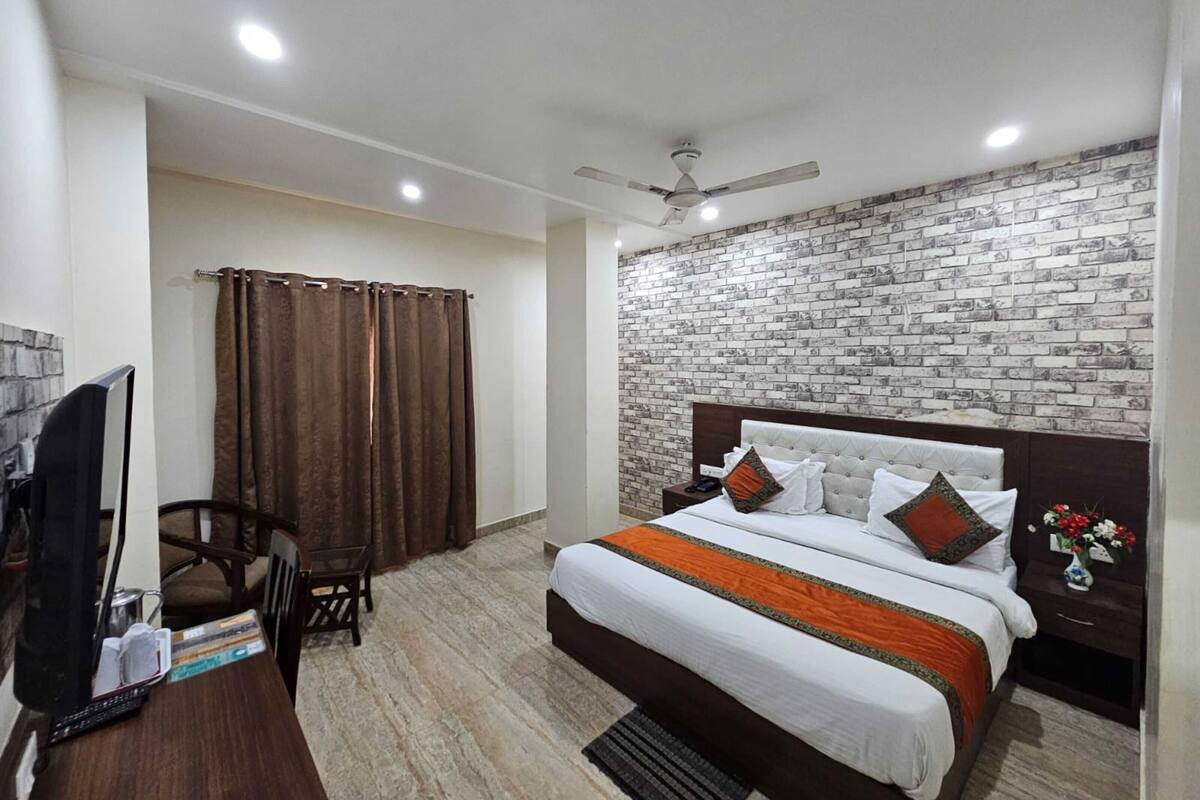Habitación de hotel con cama, escritorio, silla, televisor y pared con diseño de ladrillo.