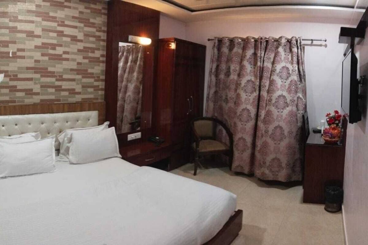 Un dormitorio con una cama grande, un armario de madera, una silla y una mesita con un florero.