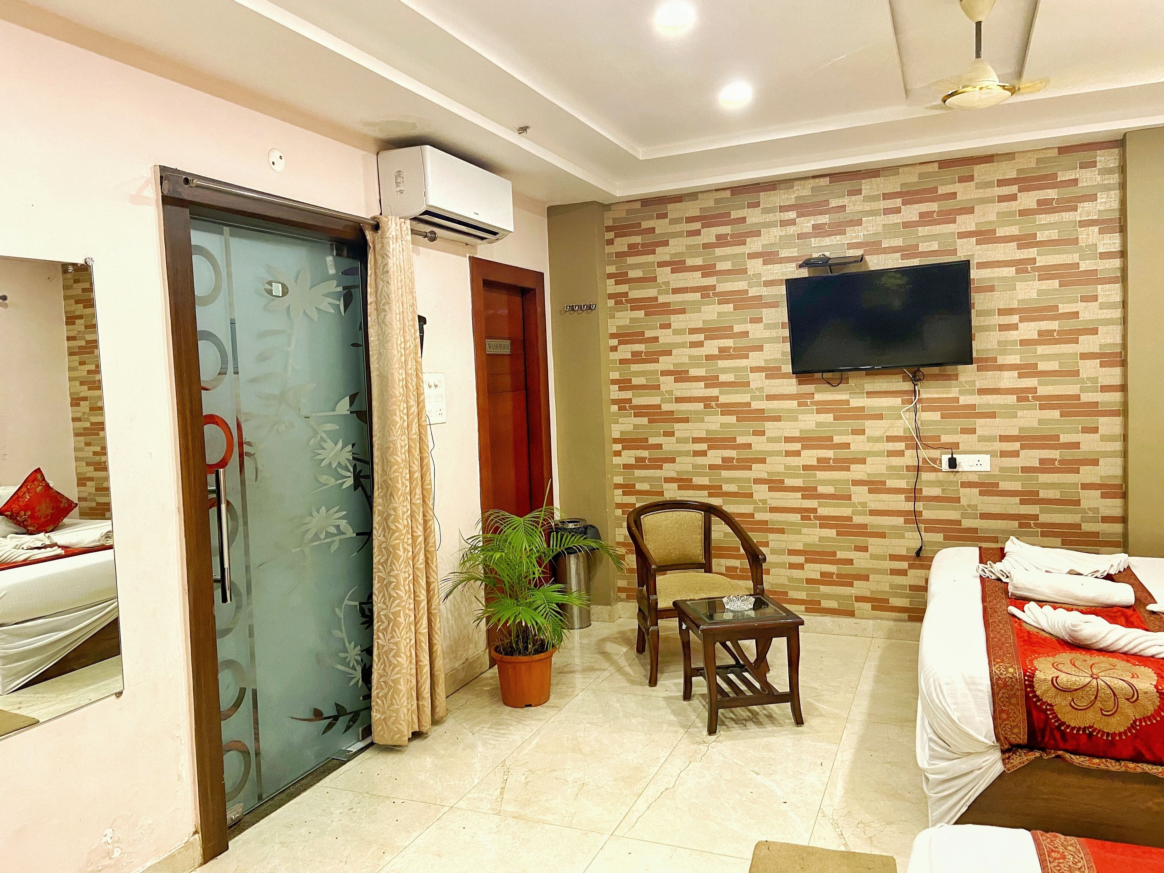 A hotel room with a bed, a TV mounted on the wall, a chair, a small table, and a potted plant.