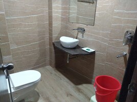 A bathroom with a toilet, a sink with a mirror above it, and a red bucket.