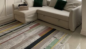 Un salon moderne avec un canapé d’angle beige, un téléviseur à écran plat, un meuble de rangement blanc et une grande fenêtre ornée de rideaux légers.