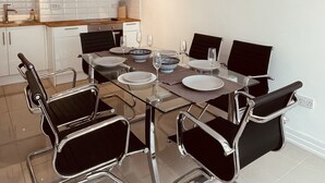 Une cuisine moderne avec des armoires blanches, une hotte de cuisinière en acier inoxydable et un coin repas comprenant une table en verre et des chaises noires.