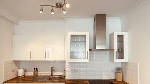 Une cuisine moderne avec des meubles blancs, un plan de travail en bois, un four encastré et une hotte en acier inoxydable.