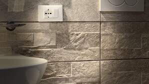 Un baño con un lavamanos grande y blanco, un interruptor de luz en la pared y una lámpara moderna.