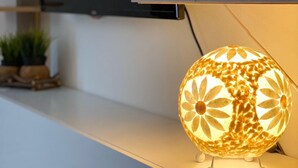 Una sala de estar moderna con un televisor de pantalla plana montado en la pared, una consola blanca y una lámpara esférica decorativa con motivos florales.