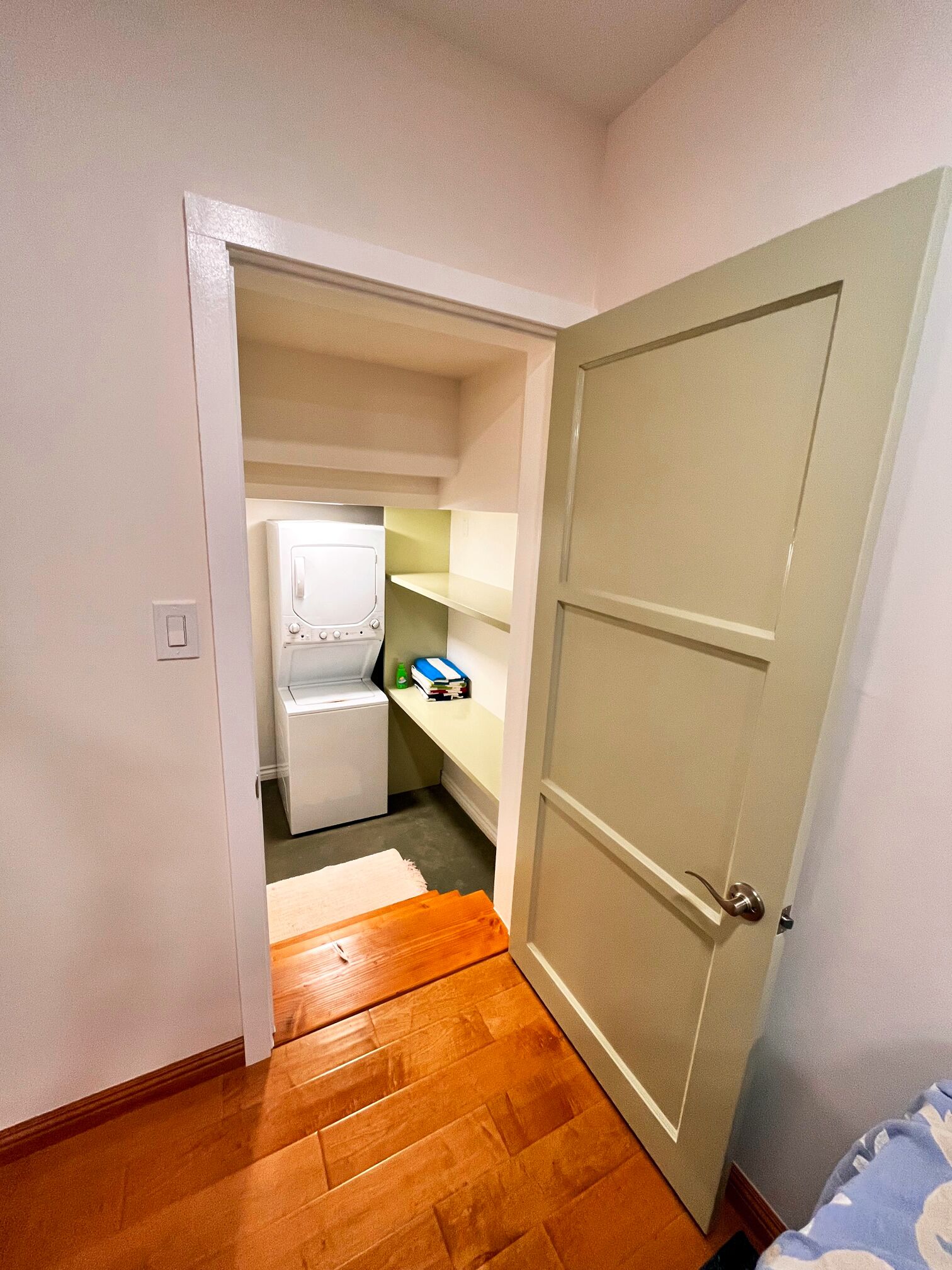 A narrow hallway leading to a laundry room with a washing machine and shelves.