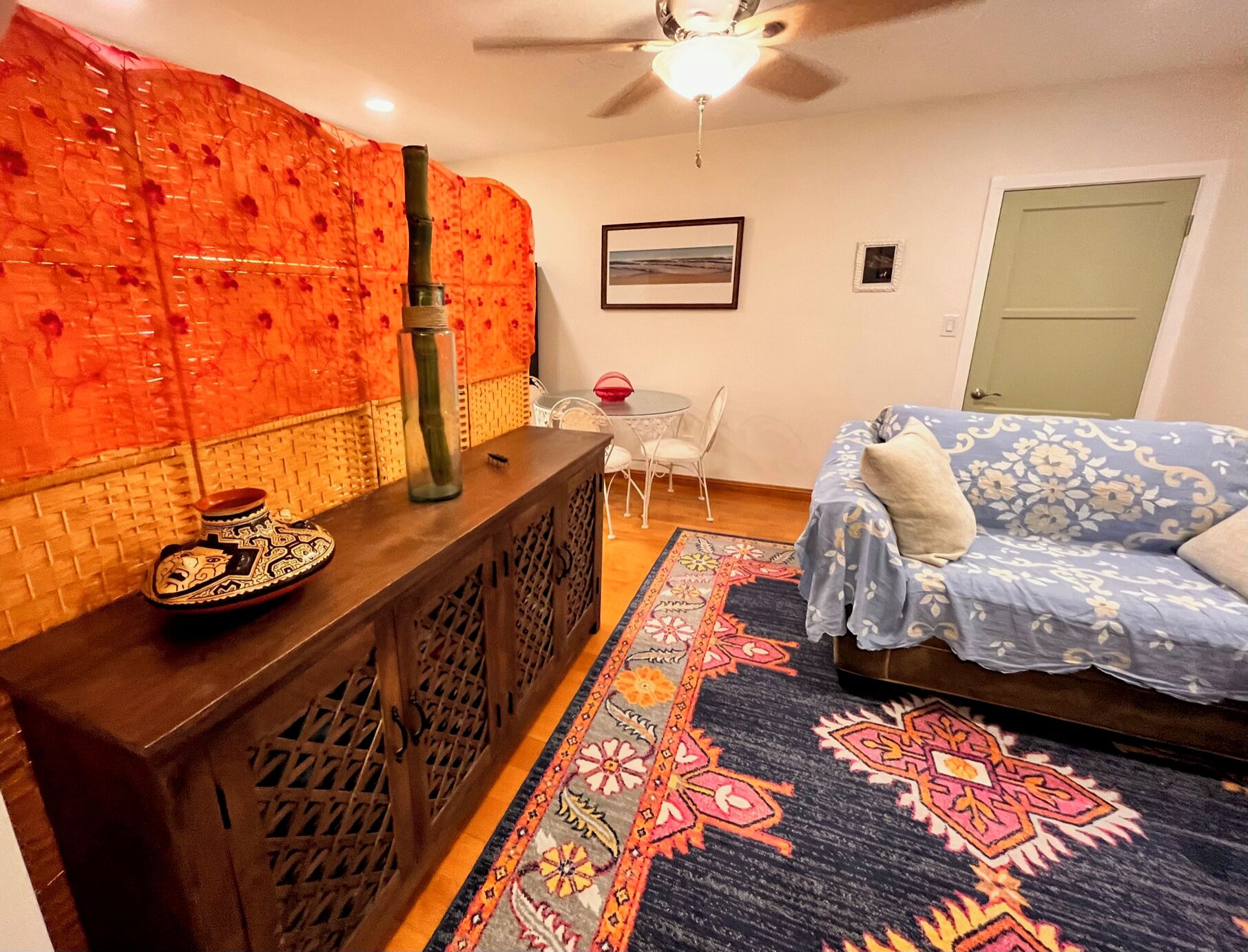 A living room with a patterned wall, a wooden sideboard, a sofa, a patterned rug, and a ceiling fan.