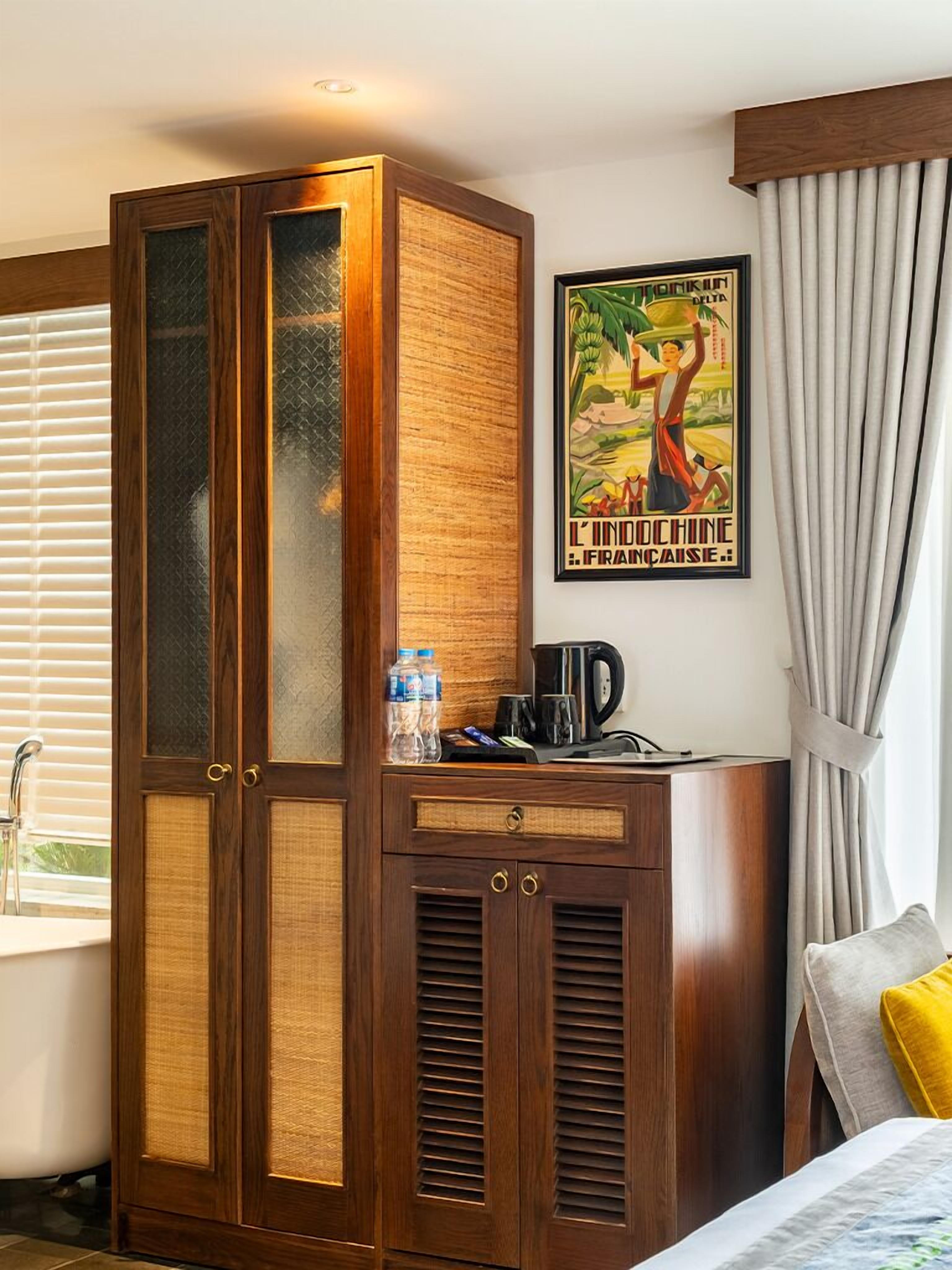 A hotel room with a wooden wardrobe, a bed, a bathroom with a sink, and a poster on the wall.