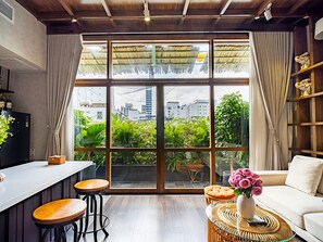A modern interior with a large window, wooden flooring, a white sofa, a wicker coffee table, and a bar area with stools.