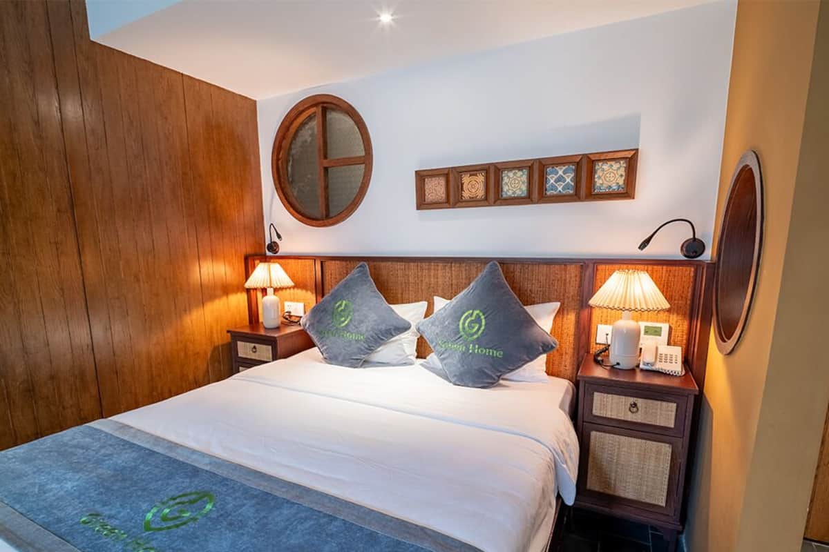 Een hotelkamer met een houten hoofdbord, een ronde spiegel, een bed met witte lakens, twee nachtkastjes met lampen en een aan de muur bevestigd telefoon.