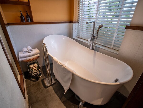 A bathroom with a freestanding bathtub, a towel rack with towels, and a window with blinds.