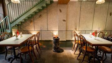 Restaurant amb una llar central, taules i cadires de fusta, i una escala verda.