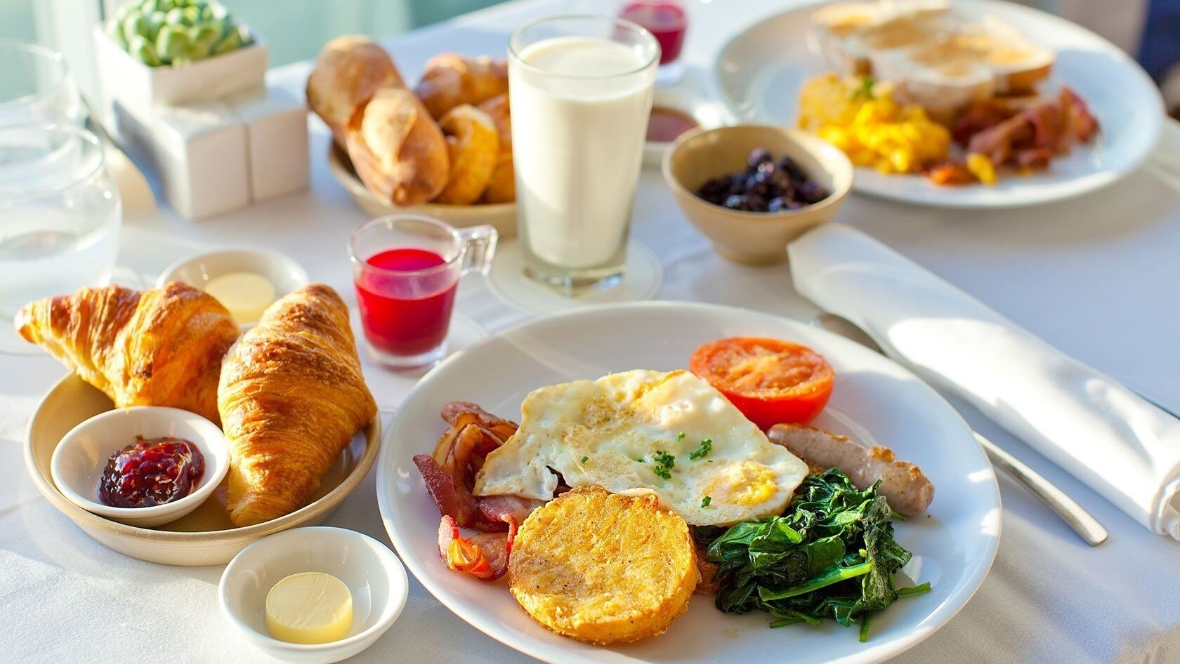 A breakfast setting with croissants, eggs, bacon, toast, and various spreads.