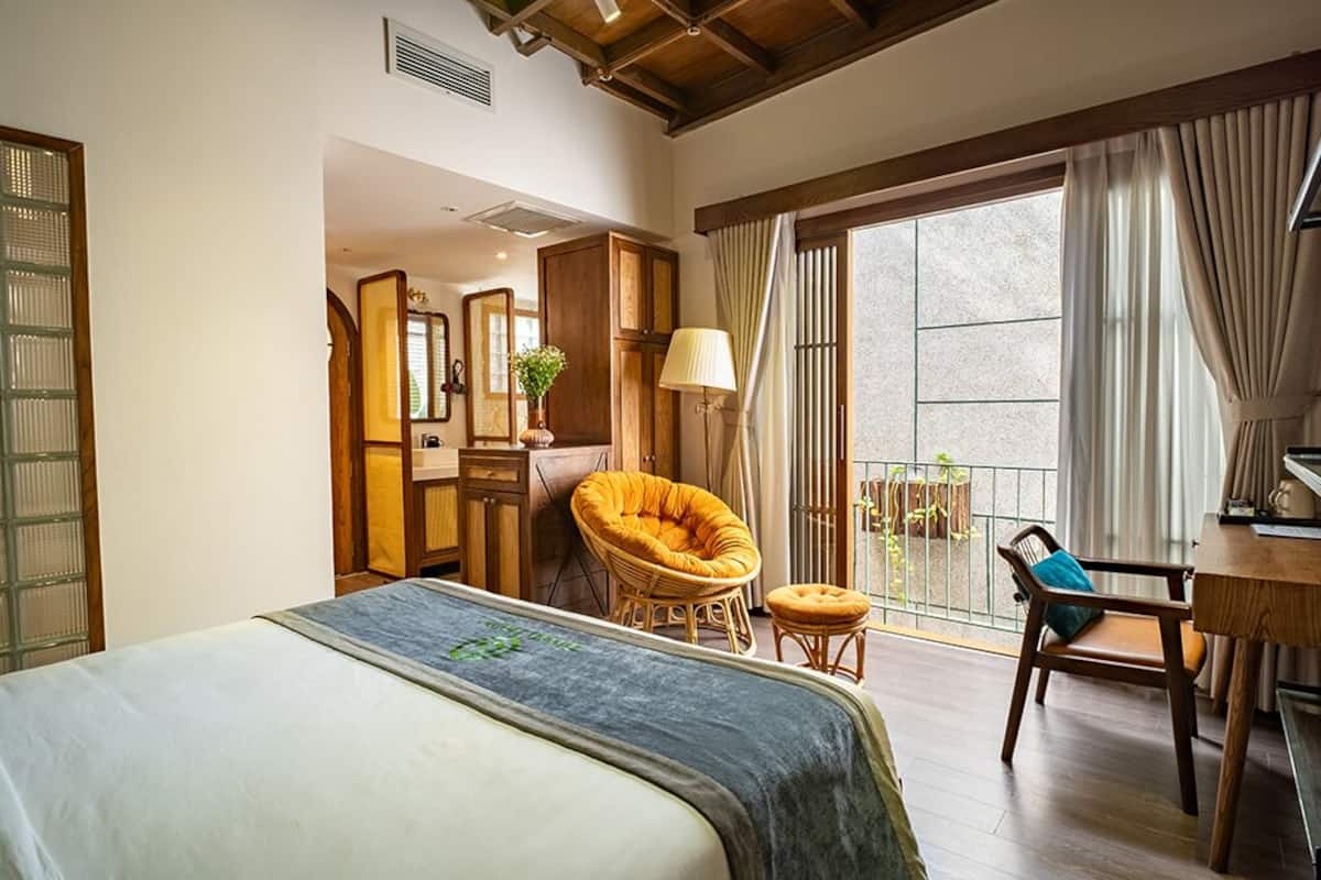 Een slaapkamer met een bed, een stoel, een bureau en een balkon met gordijnen.