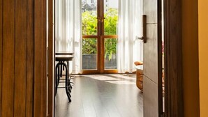Una puerta de madera abierta que da a un cuarto con una puerta de cristal, una mesita y una silla de mimbre.