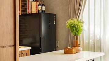 Eine moderne Küche mit einem schwarzen Kühlschrank, Holzschränken und einer weißen Arbeitsplatte. Auf der Arbeitsplatte stehen zwei Hocker und ein Blumentopf.