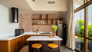 Una cocina moderna con salpicadero de ladrillo, armarios de madera, una isla grande con taburetes y vistas a zonas verdes a través de un ventanal.