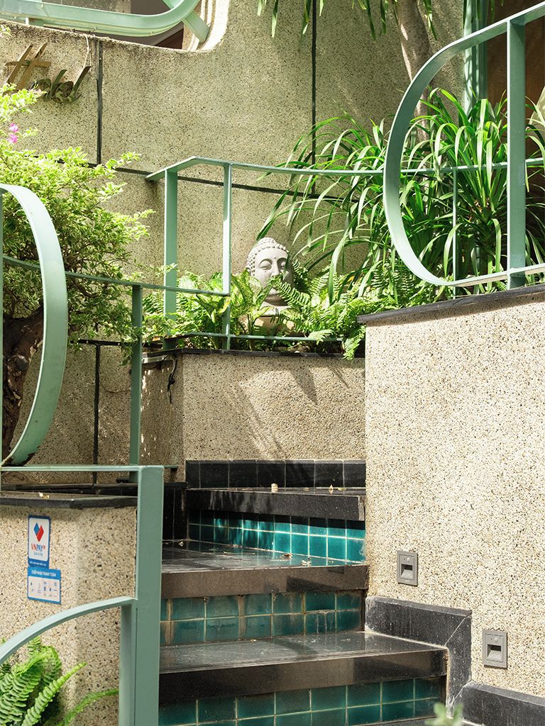 Uma escadaria com corrimãos verdes, uma estátua de Buda e uma área de piscina com azulejos.