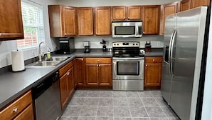 A modern kitchen with wooden cabinets, stainless steel appliances, and a dishwasher. - 4 Bedroom House with Game Room (Lexington)