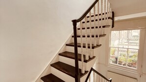 Un escalier aux marches en bois foncé et aux balustrades blanches, menant à un palier doté d’une fenêtre donnant sur un jardin.